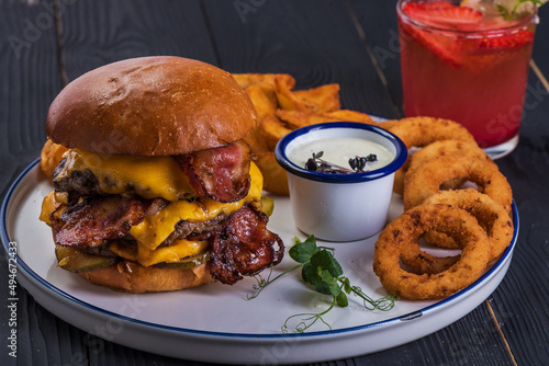 Huge burger with onion rings and garlic sauce on black wooden background