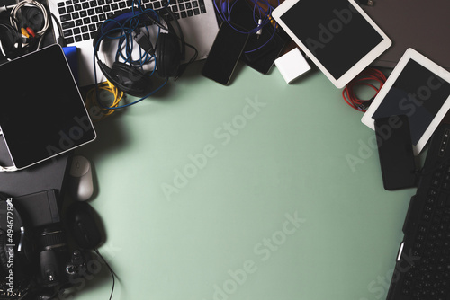 Top view to old laptop computers, digital tablets, mobile phones, many used electronic gadgets devices on green background. Planned obsolescence, electronic waste for recycling concept