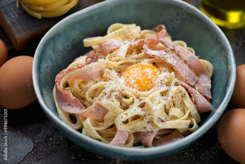 Middle closeup of italian pasta carbonara served with an egg yolk in a green bowl, horizontal shot, selective focus