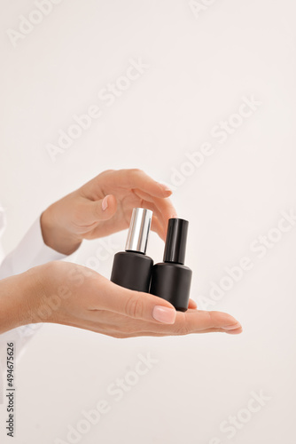 the girl holds two jars of nail polish in her hands; two black cans of nail polish are placed on the palm of her hand; black tubes of nail polish