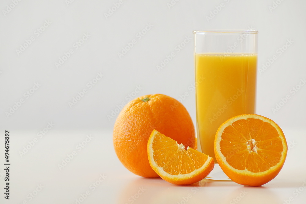 A horizontal photo showing a glass of freshly squeezed orange juice and fresh and juicy oranges themselves - whole, half and quarter. Energizing, enriched with vitamin C, the perfect start to the day A horizontal photo showing a glass of freshly squeezed orange juice and fresh and juicy oranges themselves - whole, half and quarter. Energizing, enriched with vitamin C, the perfect start to the day
