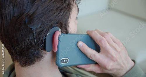 a man with a cochlear implant, with a hearing aid, speaks on a mobile phone at home