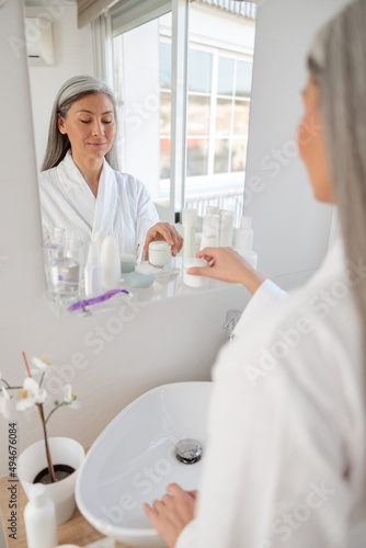 Asian woman in white bathrobe in washroom near sink