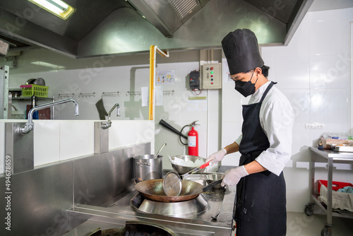 Asian male chef cook wearing face protective medical mask for protection from virus disease cooking food in frying pan at restaurant kitchen.