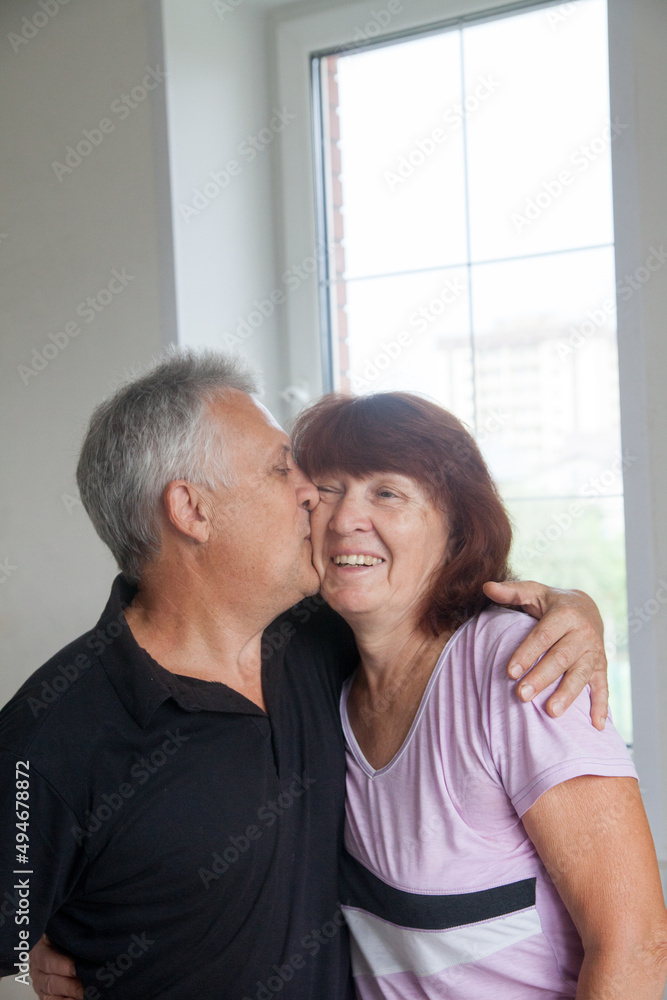 Elderly couple in casual clothes at light window of country house. Elderly couple in casual clothes at light window of country house.