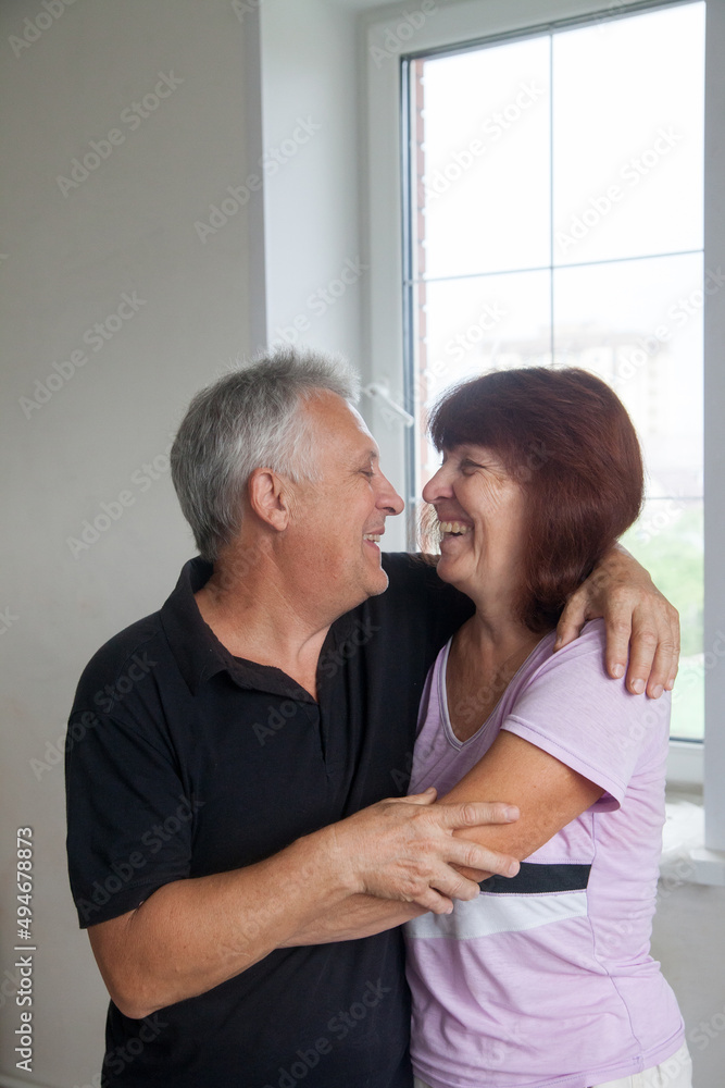Elderly couple in casual clothes at light window of country house. Elderly couple in casual clothes at light window of country house.
