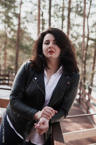  Young stylish woman wearing leather jacket  walking  in park. © DariaTrofimova