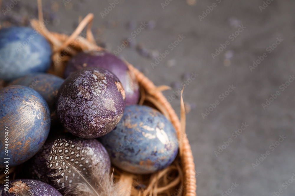 Purple, blue and golden eggs in a basket on a dark background. The purple hue trend of 2022 is very peri. Natural dye karkade tea. Top view. Easter card with a copy of the place for the text.