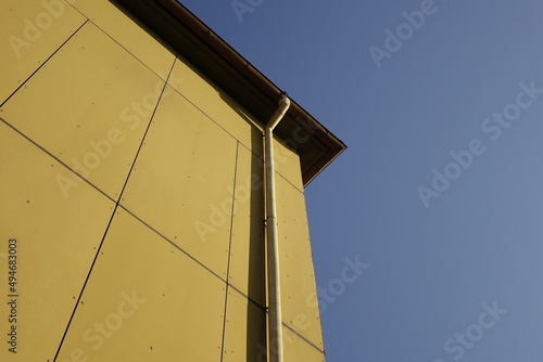 Upper right corner of dark yellow house wall with rain gutter, German 70s design, clear blue sky, use: copy space, texture, background (horizontal), Kaiserslautern, RLP, Germany