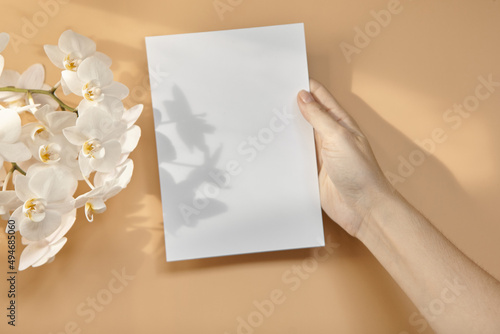 Hands are holding an empty white A5 form on a beige background. Layout top view