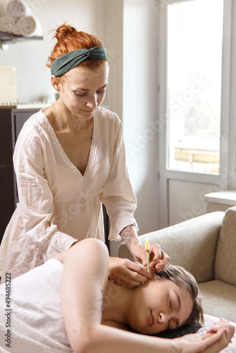 Beautiful woman receiving ear candle treatment. Therapist performing an ear wax treatment on a patient using candling. Naked woman receiving ear candle treatment from masseur