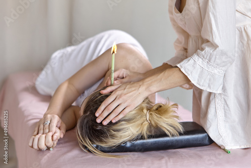 Beautiful woman receiving ear candle treatment. Therapist performing an ear wax treatment on a patient using candling. Naked woman receiving ear candle treatment from masseur
