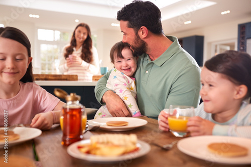 Family With Down Syndrome Daughter Sitting Around Table At Home Eating Breakfast