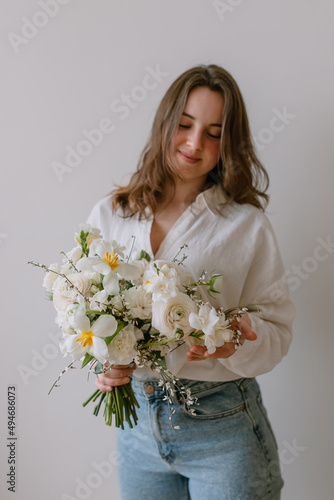 Young woman holds a bouquet of flowers in her hands. On the body is a white festive shirt.