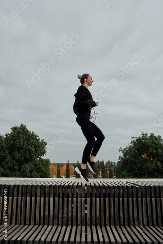 Middle-aged blonde caucasian woman athlete lady wears black tracksuit, in city park run. Workout sport outdoors.