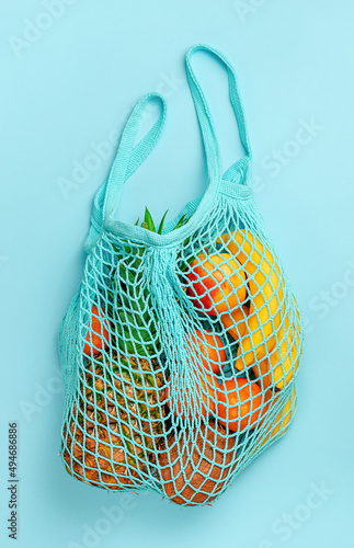 Organic fruits in reusable net bag on blue background. Top view.