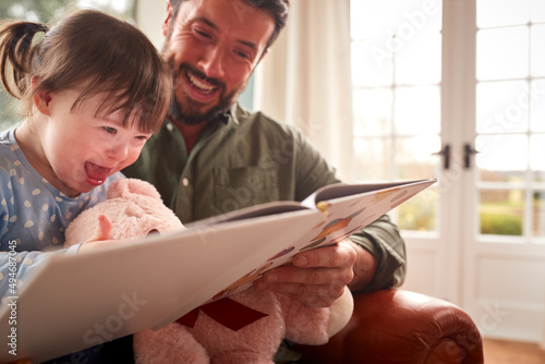 Father With Down Syndrome Daughter Reading Book At Home Together photo