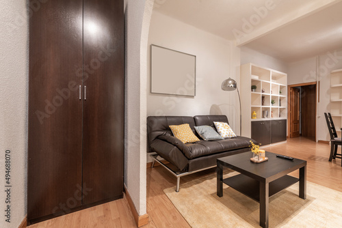 Living room hall with entrance to living room with a leather sofa with matching square dining table and white wooden shelf