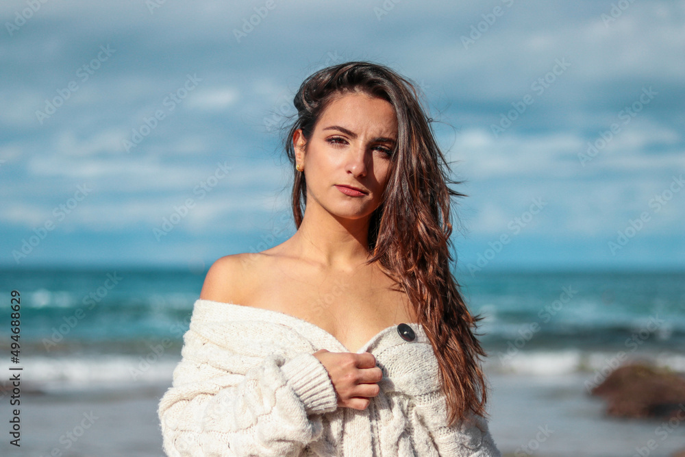 Beautiful and brunette woman looking to the camera on the beach in a sweater Beautiful and brunette woman looking to the camera on the beach in a sweater