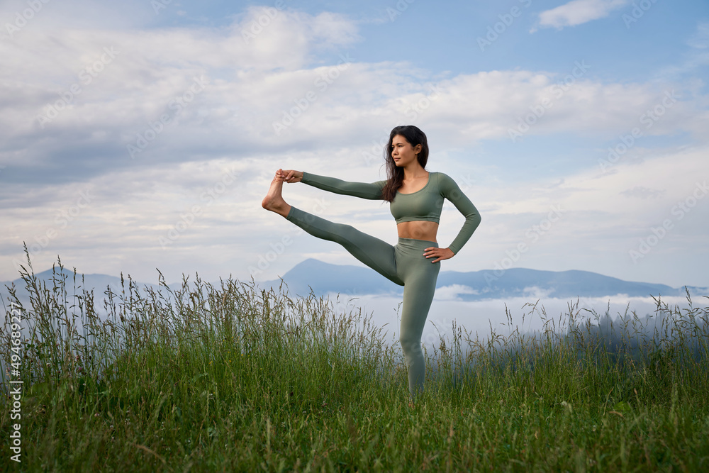 Young sporty woman dressed in activewear practising in stretching workout among summer mountains. Morning time for active training. Healthy lifestyles. Young sporty woman dressed in activewear practising in stretching workout among summer mountains. Morning time for active training. Healthy lifestyles.