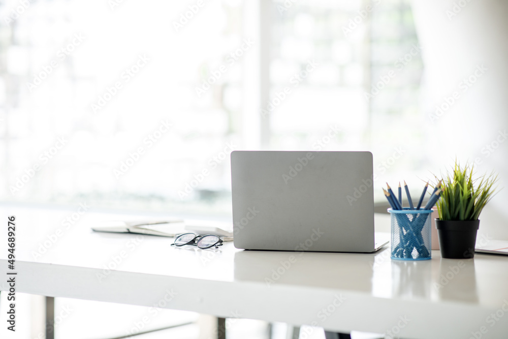 Laptop Computer, notebook, and eyeglasses sitting on a desk in a large open plan office space after working hours Laptop Computer, notebook, and eyeglasses sitting on a desk in a large open plan office space after working hours