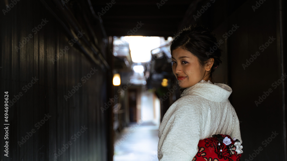 Fototapeta premium 京都、祇園の小さな路地で和服を着て微笑み振り返る日本人女性。バストアップショット