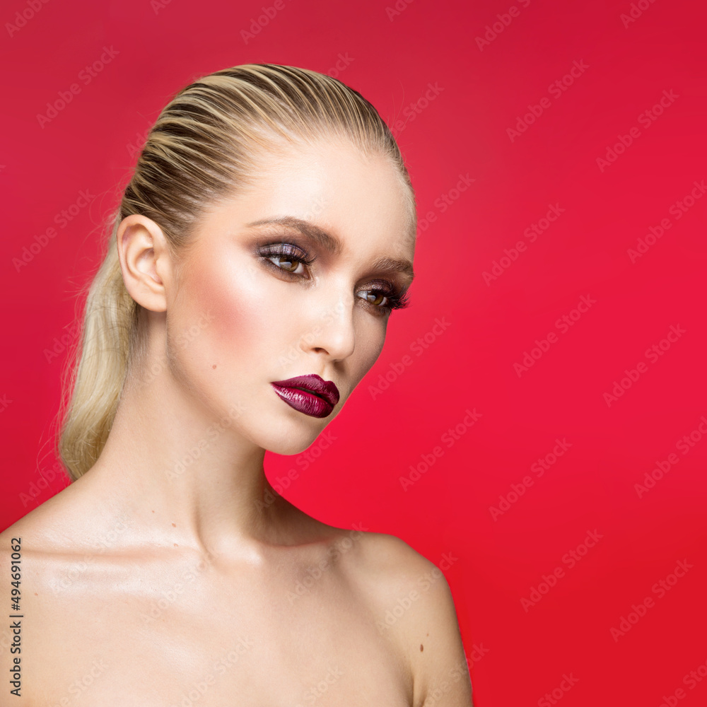 Fototapeta premium Closeup portrait of young female model with perfect makeup with bare shoulders, isolated on a red background.