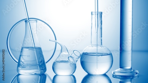 Lab glassware on reflective surface against pale blue background | Abstract skin care cosmetics formulation concept