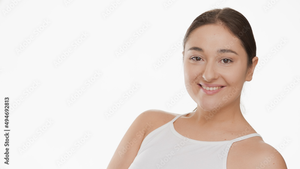 Young good-looking Caucasian brunette plus size woman in white top turns to the camera and smiling wide on white background | Smooth face concept Young good-looking Caucasian brunette plus size woman in white top turns to the camera and smiling wide on white background | Smooth face concept
