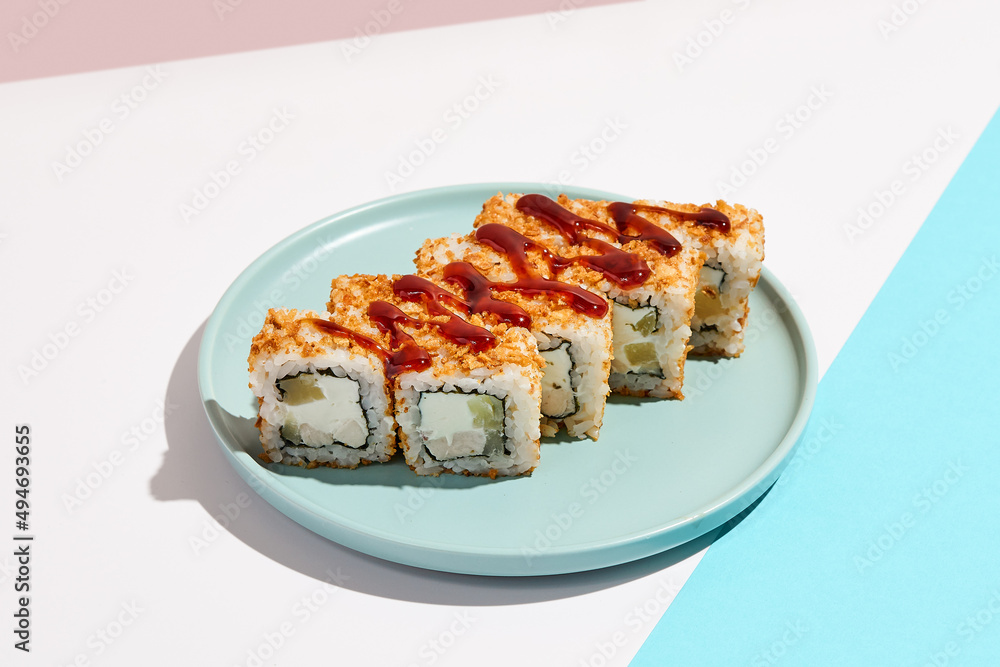 Sushi roll with chicken, cucumber and cheese inside, crispy onion outside. Maki sushi with chicken on ceramic dish. Alternative maki sushi  on coloured background in minimal style. Sushi no fish.