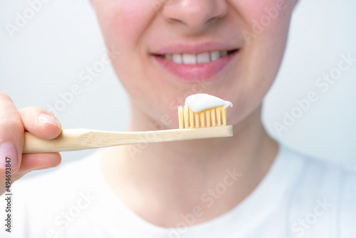 Girl holding bamboo toothbrush with toothpaste on white background, selective focus.