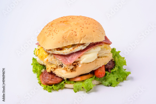 Big hamburger sandwich with smoked ham, cheese, eggs, sausage, bacon, lettuce and tomato on white background.