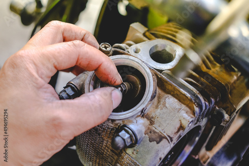 The mechanic is setting the valve on the motorcycle engine.