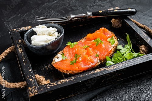 Sandwich with salmon fillet and cream cheese in wooden tray. Black background. Top view