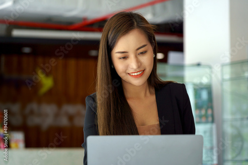 Young beautiful Asian joyful woman smiling while working with laptop in office.