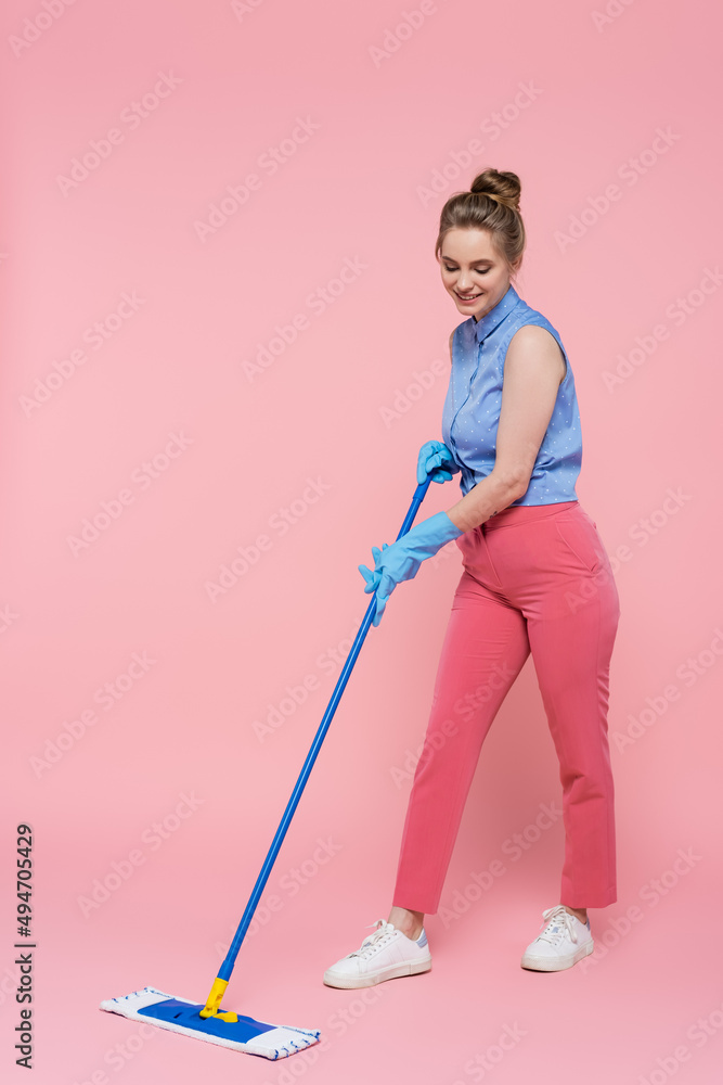full length of smiling young woman in rubber gloves cleaning with mop on pink. full length of smiling young woman in rubber gloves cleaning with mop on pink.