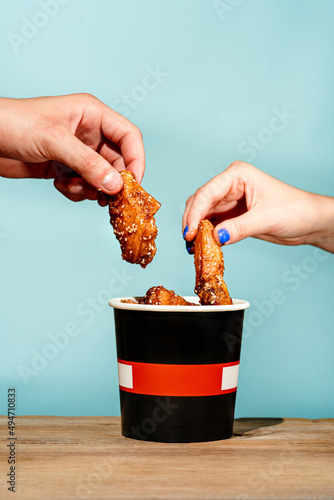 Hands pulling Fried chicken wings in a cardboard bucket mockup. Wooden table and blue background