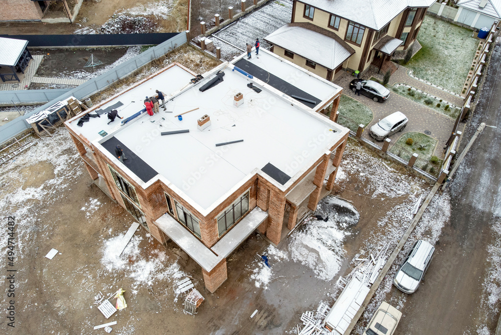 Roofing construction worker installing a flat roof. Bright blue sky in ...