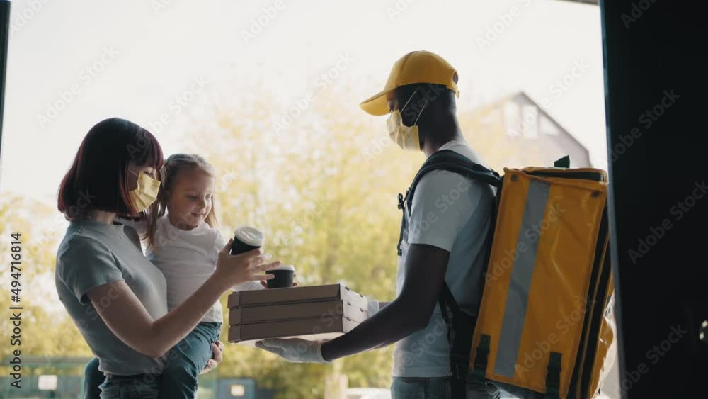 Beautiful young smiling woman with a child at the door of her house and meets a pizza delivery man who gives her cardboard boxes full of delicious steamed pizza. Food delivery man. Beautiful young smiling woman with a child at the door of her house and meets a pizza delivery man who gives her cardboard boxes full of delicious steamed pizza. Food delivery man.