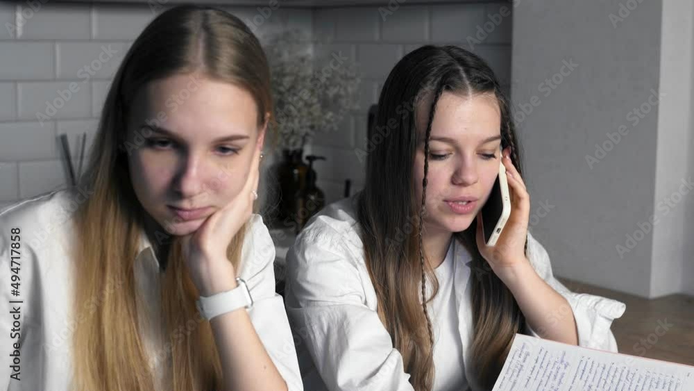 Two students are doing their homework. Close-up of one girl talking on the phone, and her friend is looking at a laptop. Study Two students are doing their homework. Close-up of one girl talking on the phone, and her friend is looking at a laptop. Study