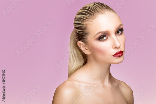 Closeup portrait of young woman with splendid makeup and hair straightened and caught in the back, isolated violet background.