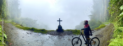Panoramic view of mountain biker near grave on edge of foggy mysterious Death Road, Bolivia
