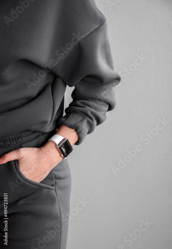 close up teen female hand with an electronic watch in gray oversize hoodie pocket near gray wall background. sport lifestyle concept, free space