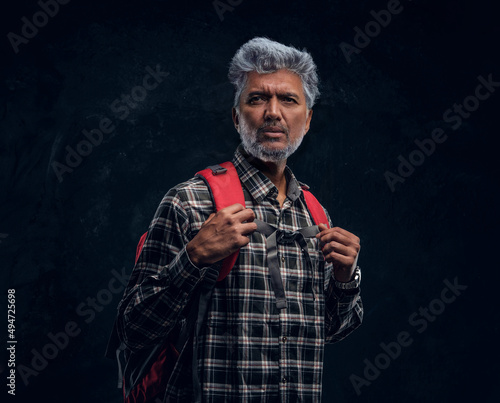 Old man tourist with red backpack against dark background © Fxquadro