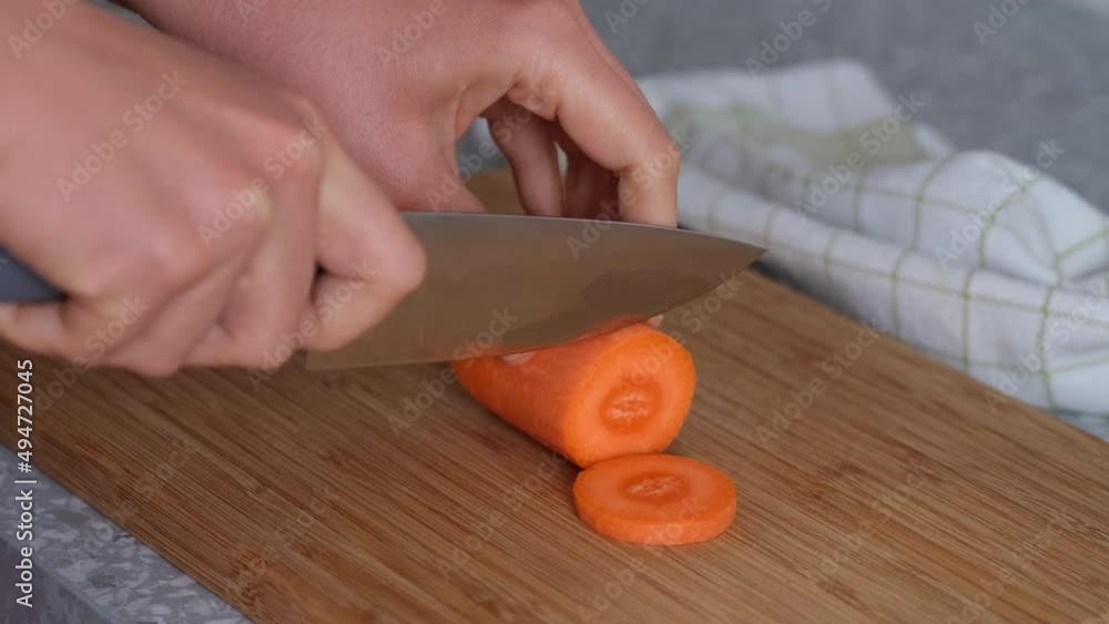 Woman cutting orange carrot on a wooden cutting board. Woman cutting orange carrot on a wooden cutting board.