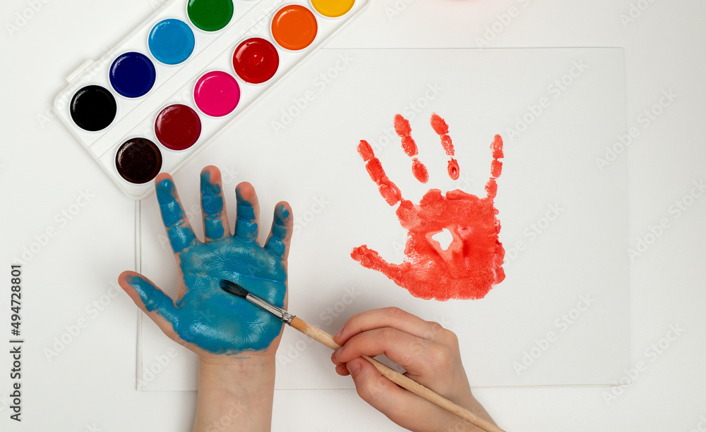 The Child Draws His Hand With Blue Paint And A Brush. Finger Painting 