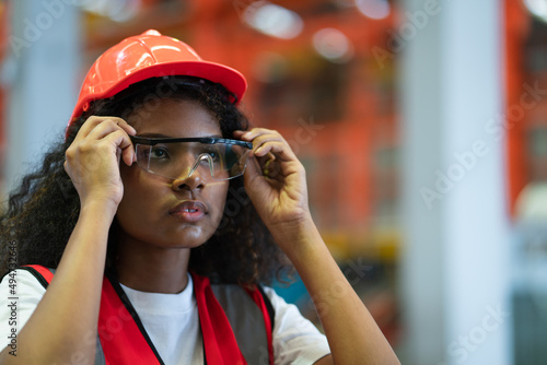 Young African American worker women in red helmet putting safety glasses for working in factory
