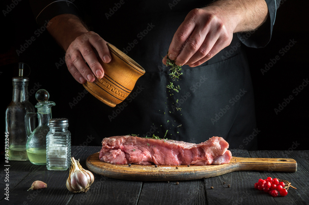 Professional chef prepares raw veal meat. Before baking, the chef adds a dry herbal seasoning to the beef. National dish is being prepared in the kitchen.