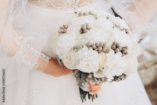 The wedding bouquet of bride in the hands on the bacground of white dress