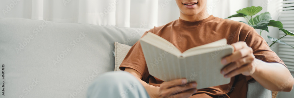 Obraz premium Young asian male reading a book in sofa Relaxation at home concept